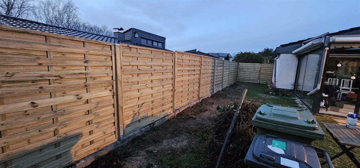 Sichtschutzzaun aus Holz mit Metallpfosten entlang eines Gartens